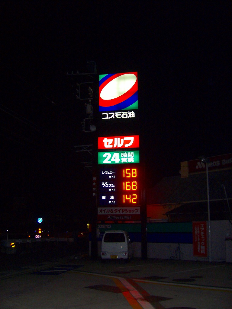 闇に浮かぶガソリンスタンドのネオン看板セルフ２４時間ガソリン単価が表示されている